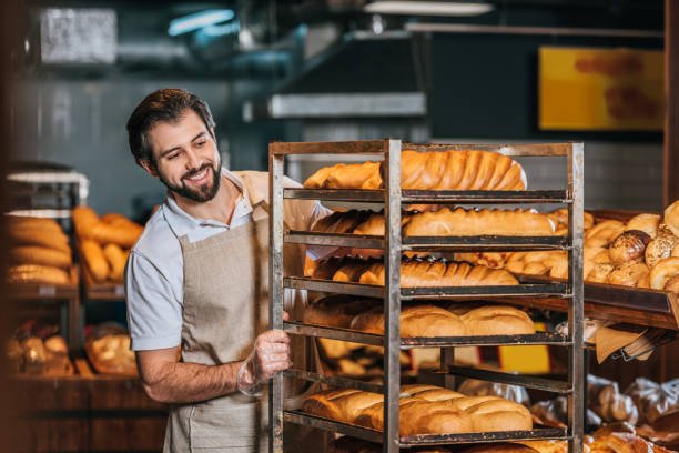 Smiling Male Shop Assistant Arranging Fresh Pastry In Supermarket - HT Contábil